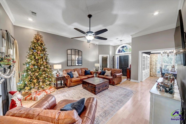 living room featuring a textured ceiling, ceiling fan with notable chandelier, light hardwood / wood-style flooring, and crown molding