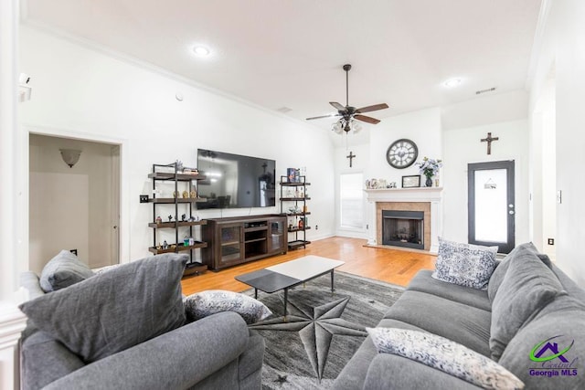 living room featuring ceiling fan, light wood-type flooring, ornamental molding, a wealth of natural light, and a tiled fireplace