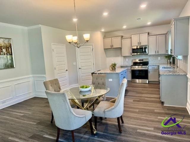 dining space with ornamental molding, a notable chandelier, dark wood-type flooring, and sink