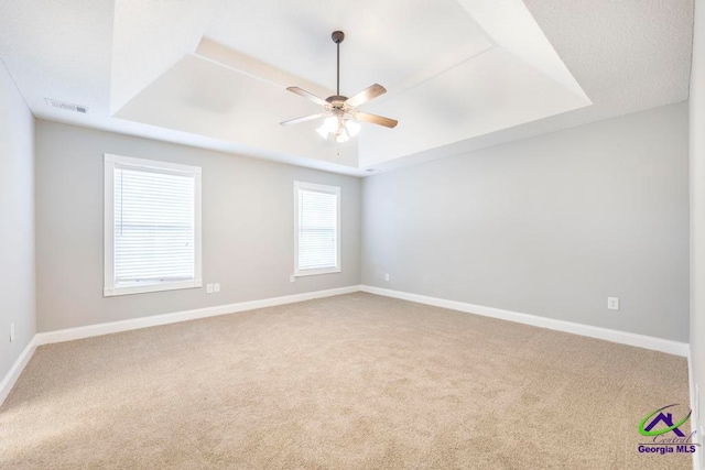 empty room with carpet flooring, a raised ceiling, and ceiling fan