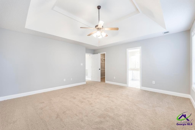 empty room with a raised ceiling, ceiling fan, and carpet flooring