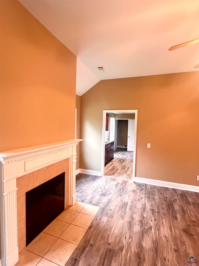 unfurnished living room with a tile fireplace, lofted ceiling, and hardwood / wood-style flooring