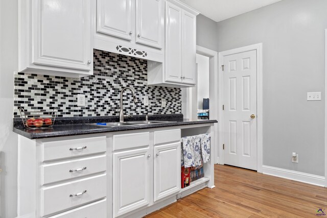 kitchen featuring decorative backsplash, dark stone counters, sink, white cabinets, and light hardwood / wood-style floors