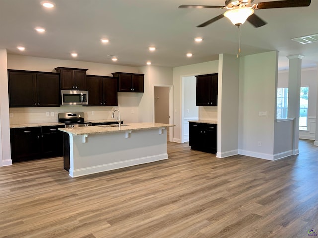 kitchen with light stone countertops, appliances with stainless steel finishes, sink, a center island with sink, and light hardwood / wood-style floors