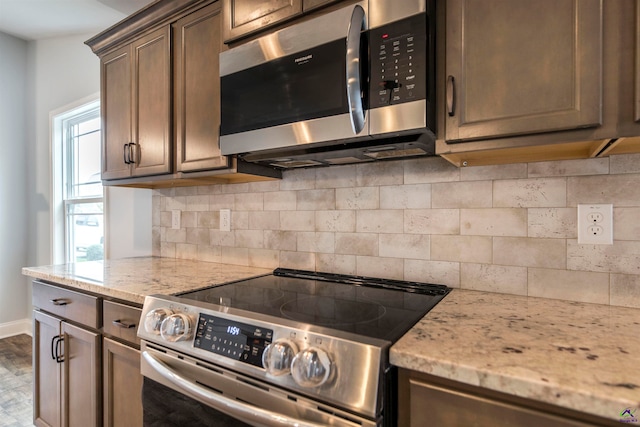 kitchen featuring decorative backsplash, wood-type flooring, light stone countertops, and stainless steel appliances