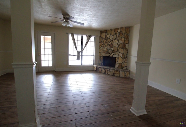 unfurnished living room with a textured ceiling, a stone fireplace, ceiling fan, and dark wood-type flooring