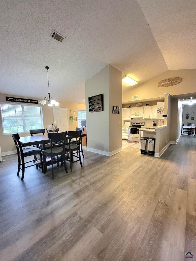 dining room with a textured ceiling, light hardwood / wood-style floors, an inviting chandelier, and lofted ceiling