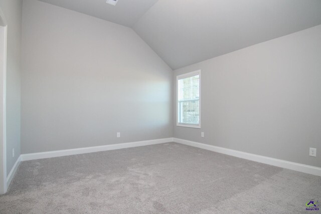 carpeted spare room with vaulted ceiling