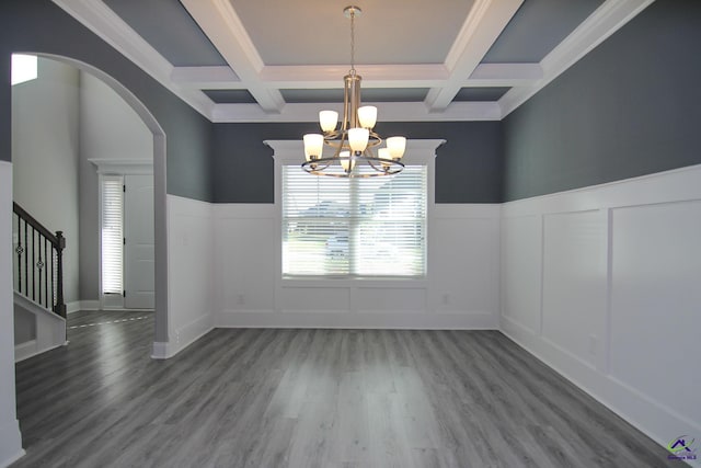 unfurnished dining area with coffered ceiling, ornamental molding, beamed ceiling, wood-type flooring, and a chandelier