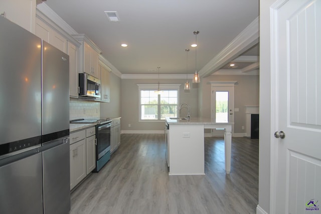 kitchen with hanging light fixtures, stainless steel appliances, crown molding, light hardwood / wood-style floors, and a kitchen island with sink