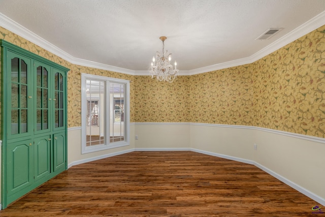 unfurnished dining area featuring a textured ceiling, dark hardwood / wood-style flooring, crown molding, and a notable chandelier