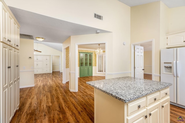 kitchen featuring white refrigerator with ice dispenser, wood-type flooring, a kitchen island, and light stone counters