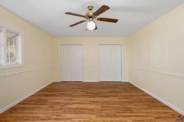 unfurnished bedroom with hardwood / wood-style flooring, ceiling fan, and multiple closets