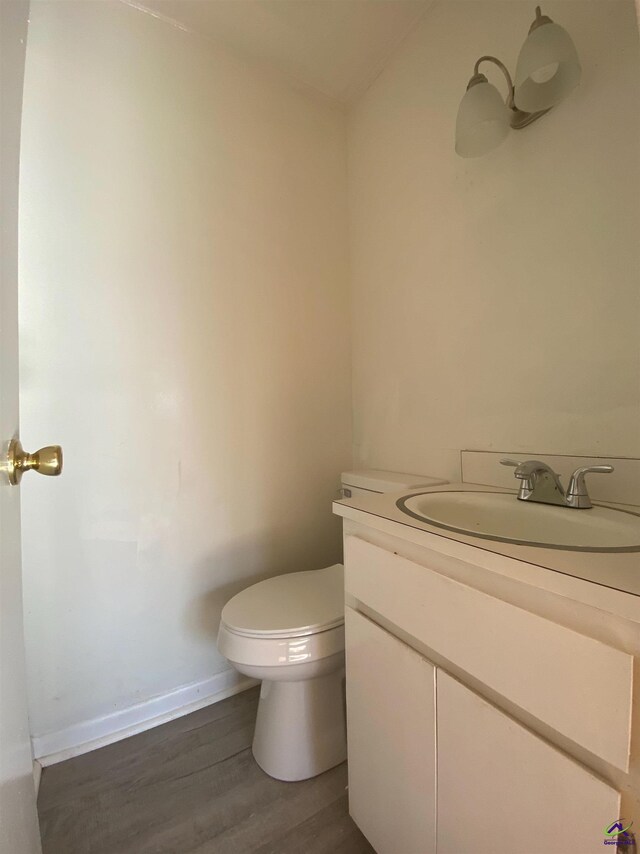 bathroom featuring baseboards, toilet, wood finished floors, and vanity