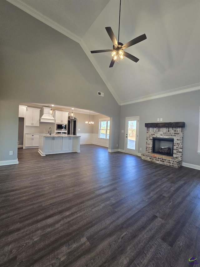 unfurnished living room featuring ceiling fan, dark wood-type flooring, high vaulted ceiling, crown molding, and a fireplace