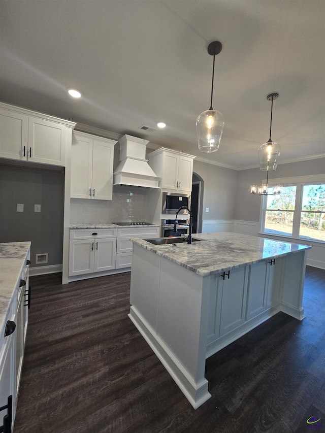 kitchen with stainless steel microwave, hanging light fixtures, stovetop, white cabinets, and custom exhaust hood