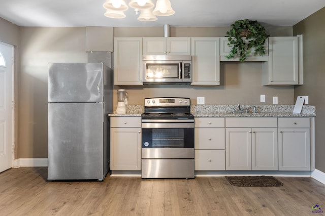 kitchen with light stone counters, stainless steel appliances, sink, light hardwood / wood-style flooring, and white cabinets