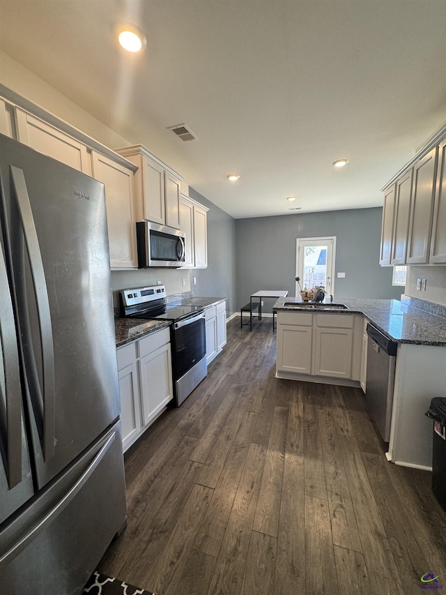 kitchen featuring dark stone counters, kitchen peninsula, stainless steel appliances, and dark hardwood / wood-style floors