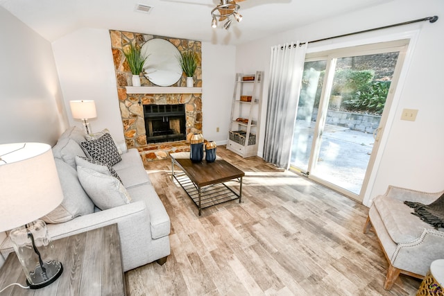 living room with a stone fireplace, ceiling fan, and light wood-type flooring