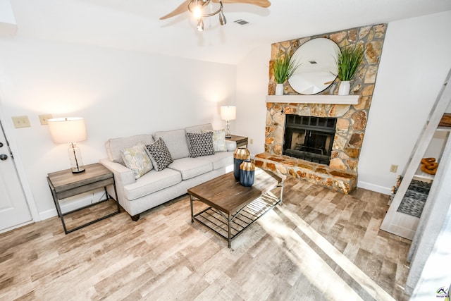 living room featuring hardwood / wood-style flooring, ceiling fan, and a stone fireplace