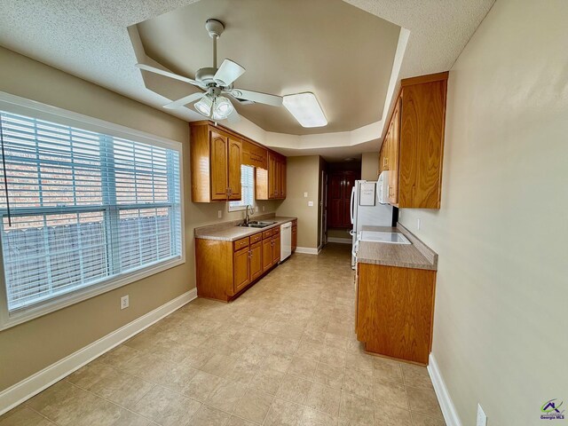 kitchen with white appliances, a raised ceiling, sink, ceiling fan, and a textured ceiling