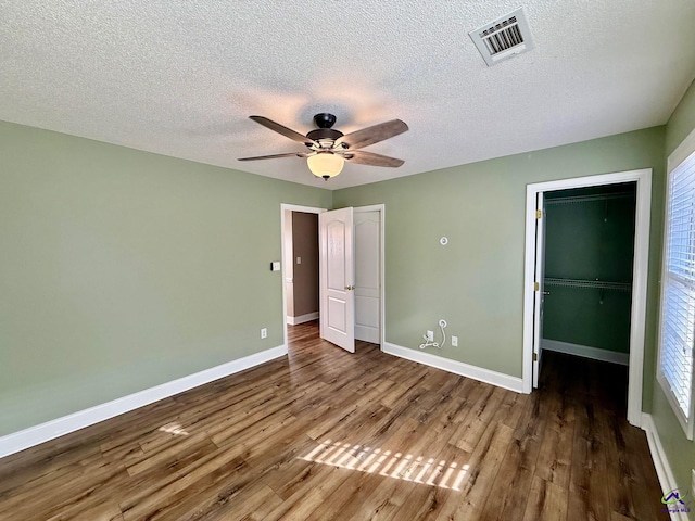 unfurnished bedroom featuring a textured ceiling, ceiling fan, a walk in closet, and dark wood-type flooring