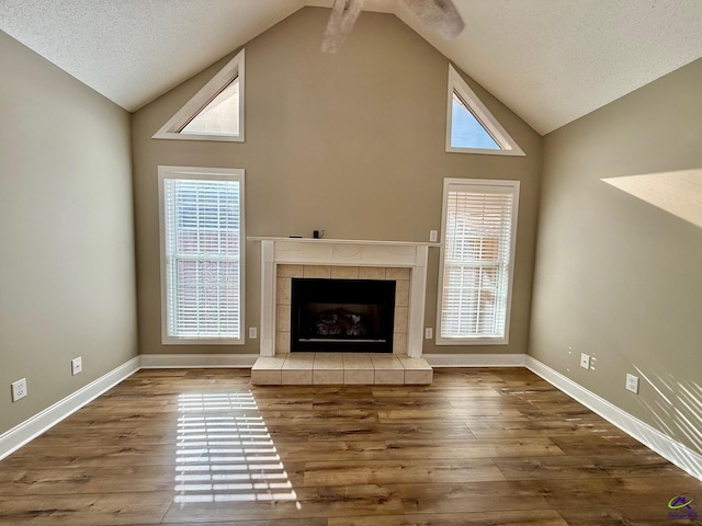 unfurnished living room with hardwood / wood-style floors, a fireplace, a textured ceiling, and high vaulted ceiling