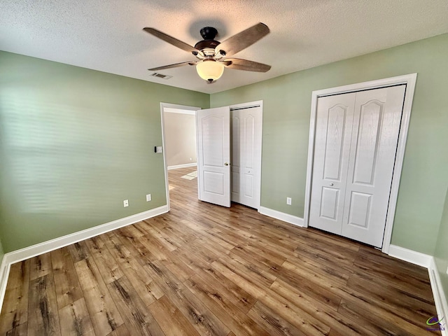 unfurnished bedroom featuring hardwood / wood-style flooring, ceiling fan, a textured ceiling, and multiple closets