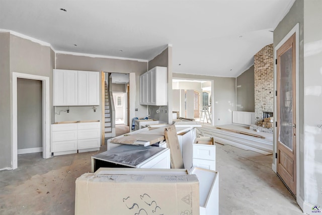 kitchen with white cabinets, crown molding, a fireplace, and vaulted ceiling