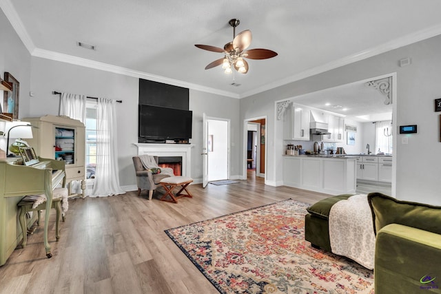 living room featuring ceiling fan, crown molding, a textured ceiling, a fireplace, and light wood-type flooring