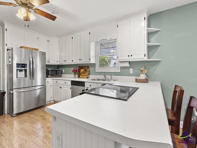 kitchen with sink, kitchen peninsula, appliances with stainless steel finishes, white cabinets, and light wood-type flooring