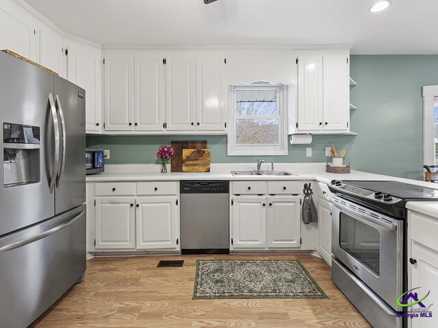 kitchen with light wood-type flooring, stainless steel appliances, white cabinetry, and sink