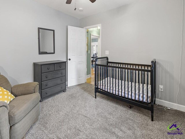 carpeted bedroom featuring ceiling fan and a nursery area