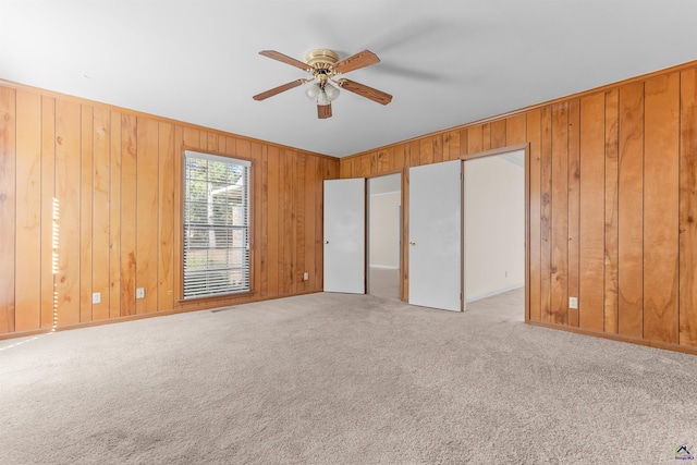 unfurnished bedroom featuring light carpet, ceiling fan, and wooden walls