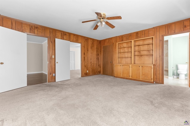 interior space with wood walls, built in shelves, ceiling fan, and light carpet