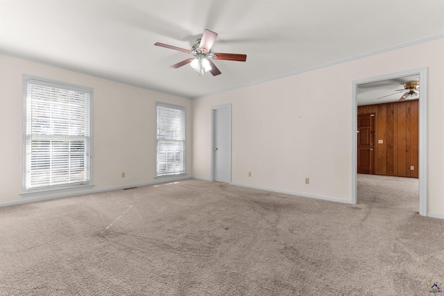 unfurnished room featuring light carpet, ceiling fan, ornamental molding, and wood walls