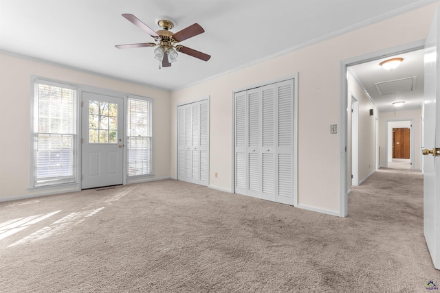 unfurnished bedroom with ceiling fan, crown molding, light carpet, and multiple closets