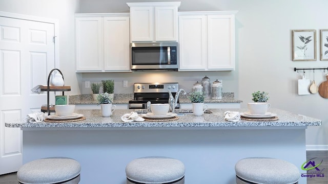 kitchen with dark hardwood / wood-style floors, white cabinetry, stainless steel appliances, and a kitchen island with sink