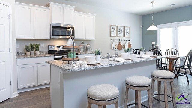 kitchen featuring appliances with stainless steel finishes, a center island with sink, white cabinets, dark hardwood / wood-style floors, and hanging light fixtures