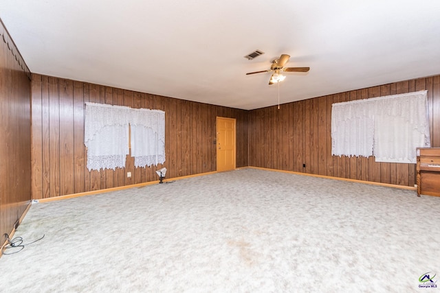 carpeted empty room featuring ceiling fan and wooden walls