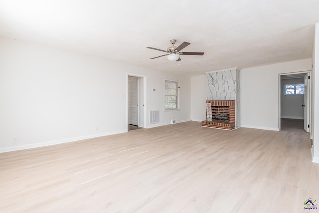 unfurnished living room with light wood-type flooring, a brick fireplace, ceiling fan, and a healthy amount of sunlight