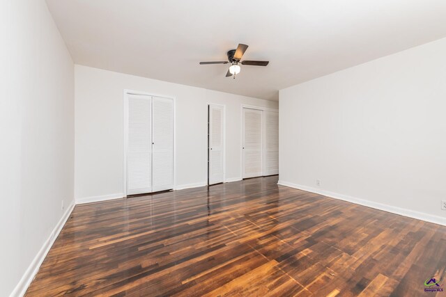 unfurnished bedroom with dark hardwood / wood-style flooring, two closets, and ceiling fan