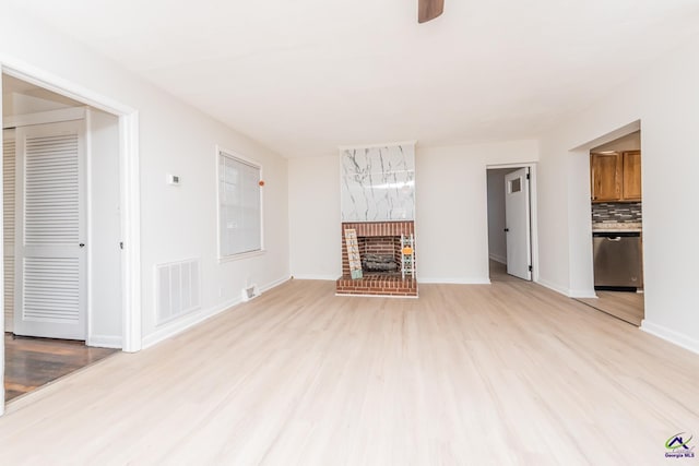 unfurnished living room with ceiling fan, light hardwood / wood-style floors, and a brick fireplace