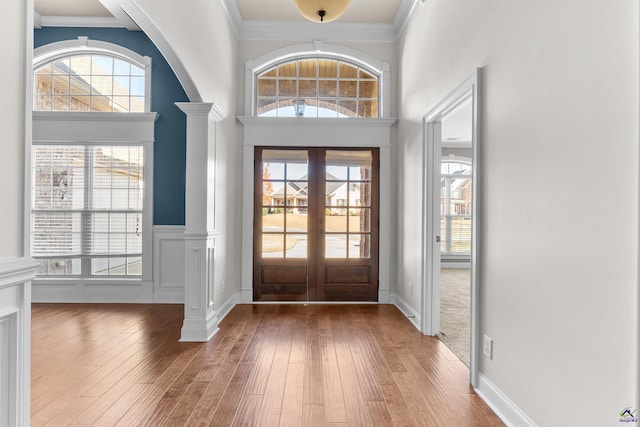 foyer entrance with decorative columns, wood-type flooring, and ornamental molding