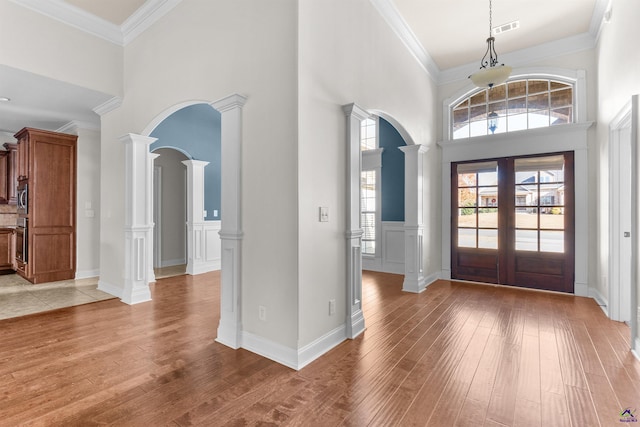 entryway with wood-type flooring, a towering ceiling, crown molding, and decorative columns