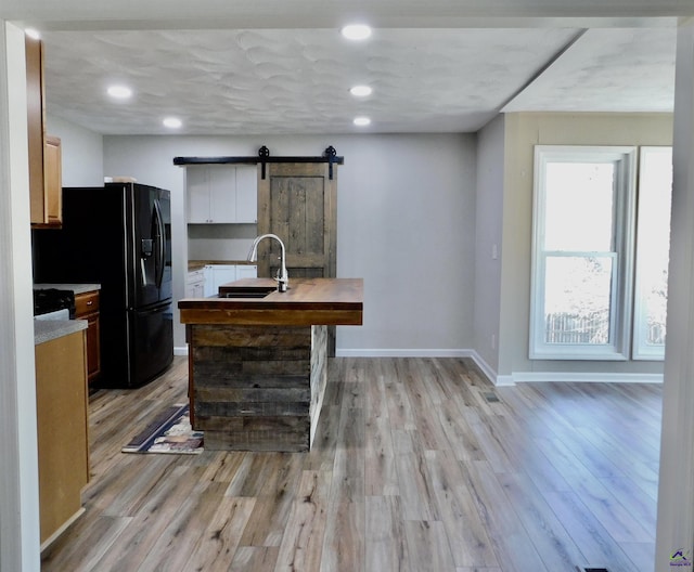 kitchen with a barn door, black refrigerator with ice dispenser, sink, and light hardwood / wood-style floors