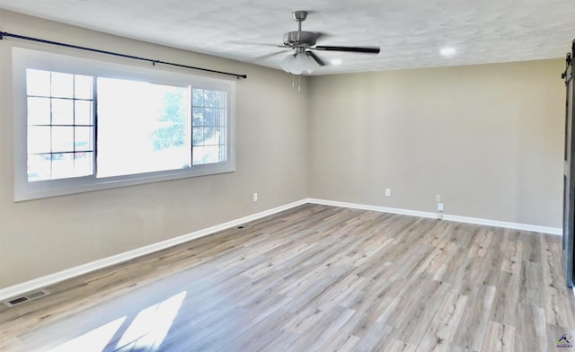 empty room with ceiling fan, light hardwood / wood-style floors, and a barn door