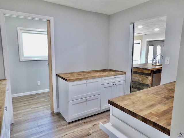 kitchen with light wood-type flooring, sink, dishwasher, white cabinetry, and butcher block counters