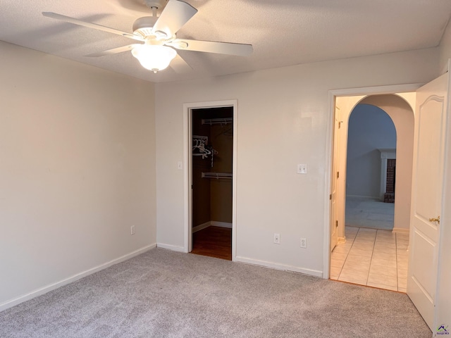 unfurnished bedroom with light carpet, a walk in closet, ceiling fan, a textured ceiling, and a closet