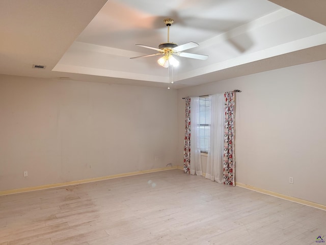 spare room with a raised ceiling, ceiling fan, and light hardwood / wood-style flooring